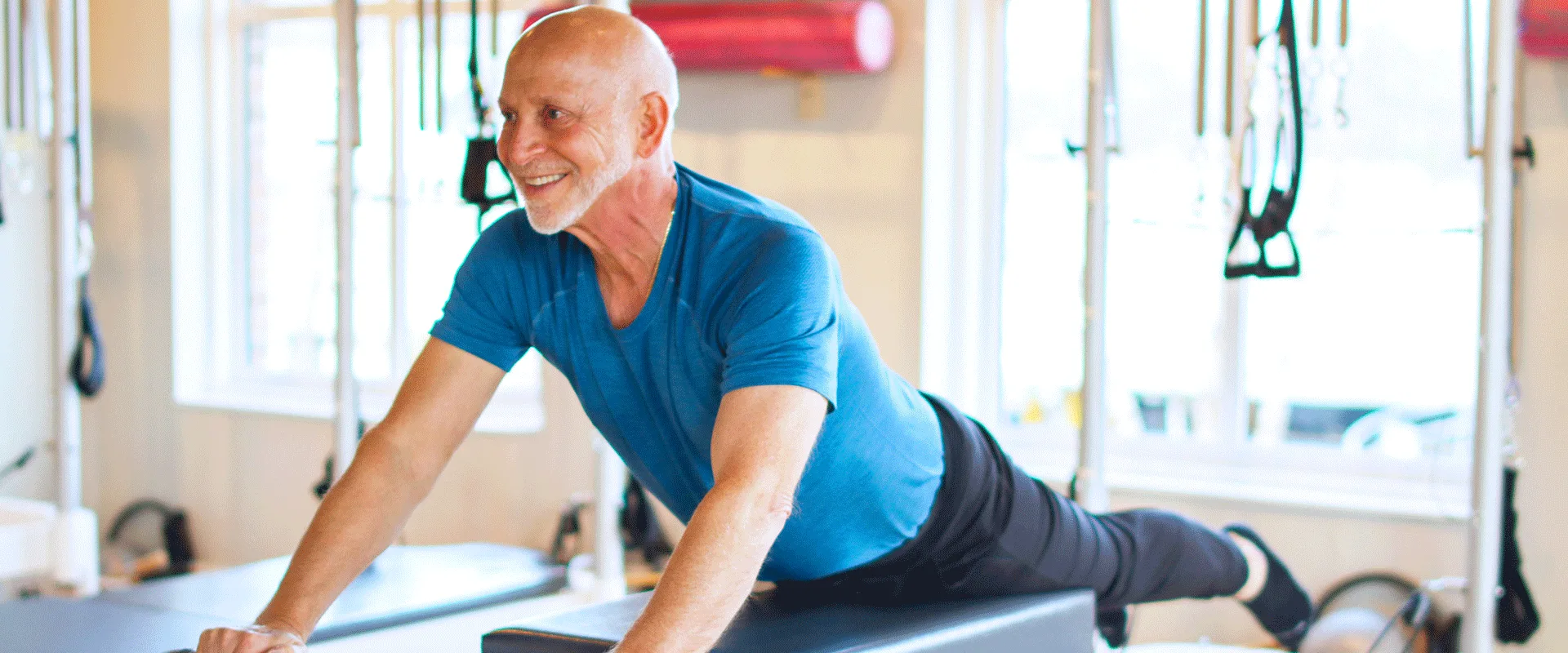 An older client smiles mid-plank on a reformer — Bovée Pilates serves all ages.