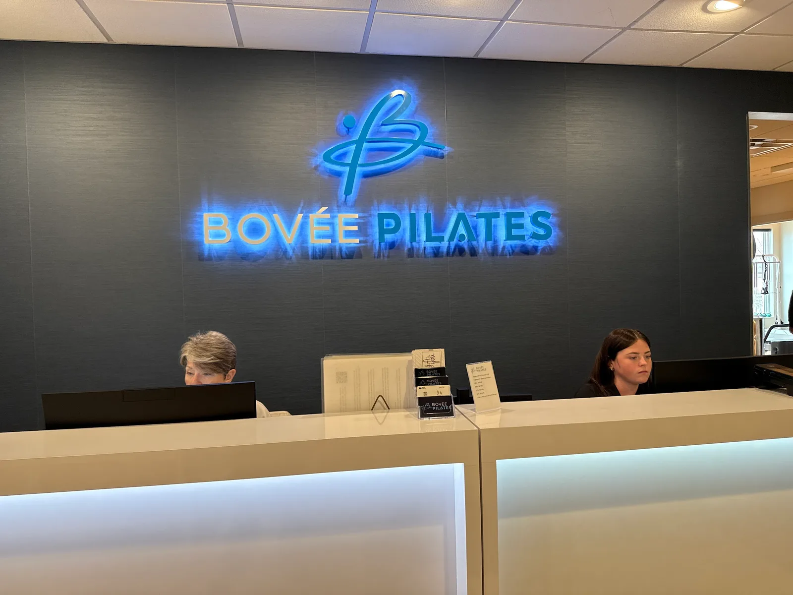 The illuminated Bovée Pilates wordmark glowing above the front desk inside the studio.
